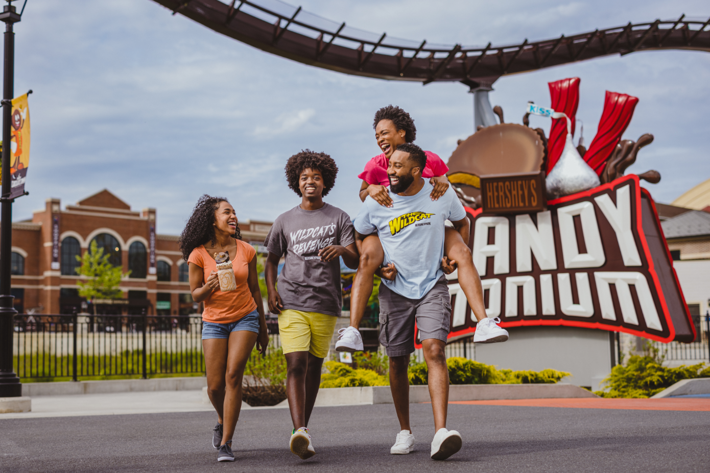 Smiling family posing with Hersheypark merch in front of the candymonium coaster sign.