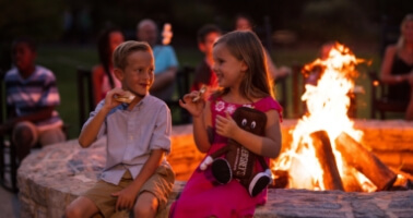 Family roasting marshmallows at firepit outside of resort