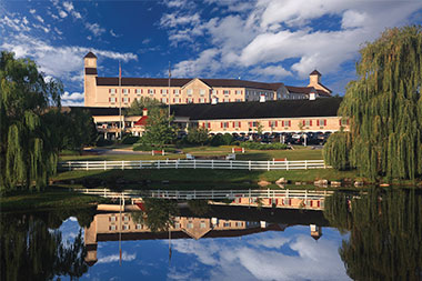 Exterior photo of the front of the Hershey Lodge on a spring day with a reflection of the lodge in the water.