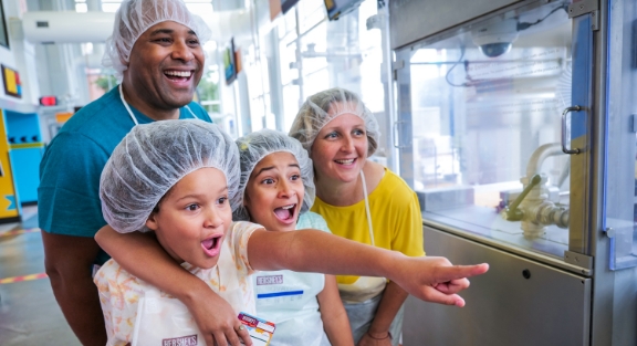 Mother and Father with their two children experiencing Create Your Own Candy Bar attraction at Hershey's Chocolate World